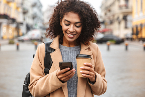 woman holding cup of coffee while looking at her cell phone 